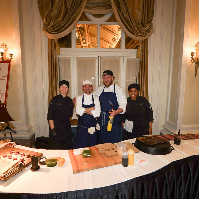 4 chefs stand behind a food station