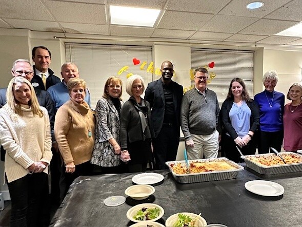 Group shot of multiple adults behind a table of food
