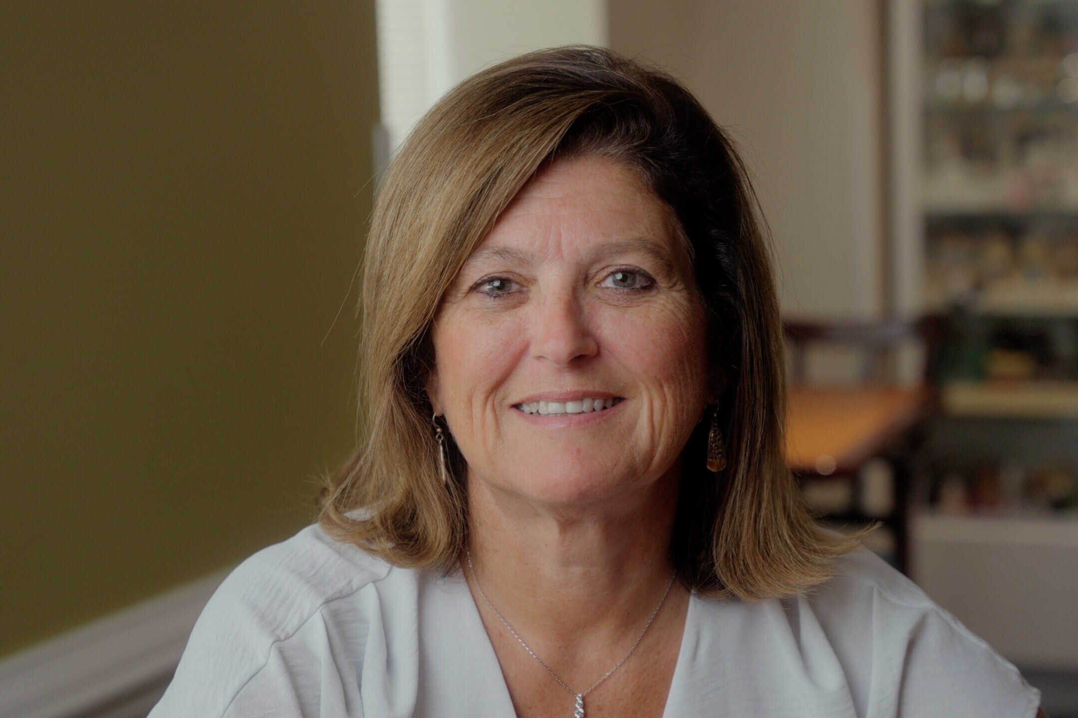 A smiling adult sits in a dining room