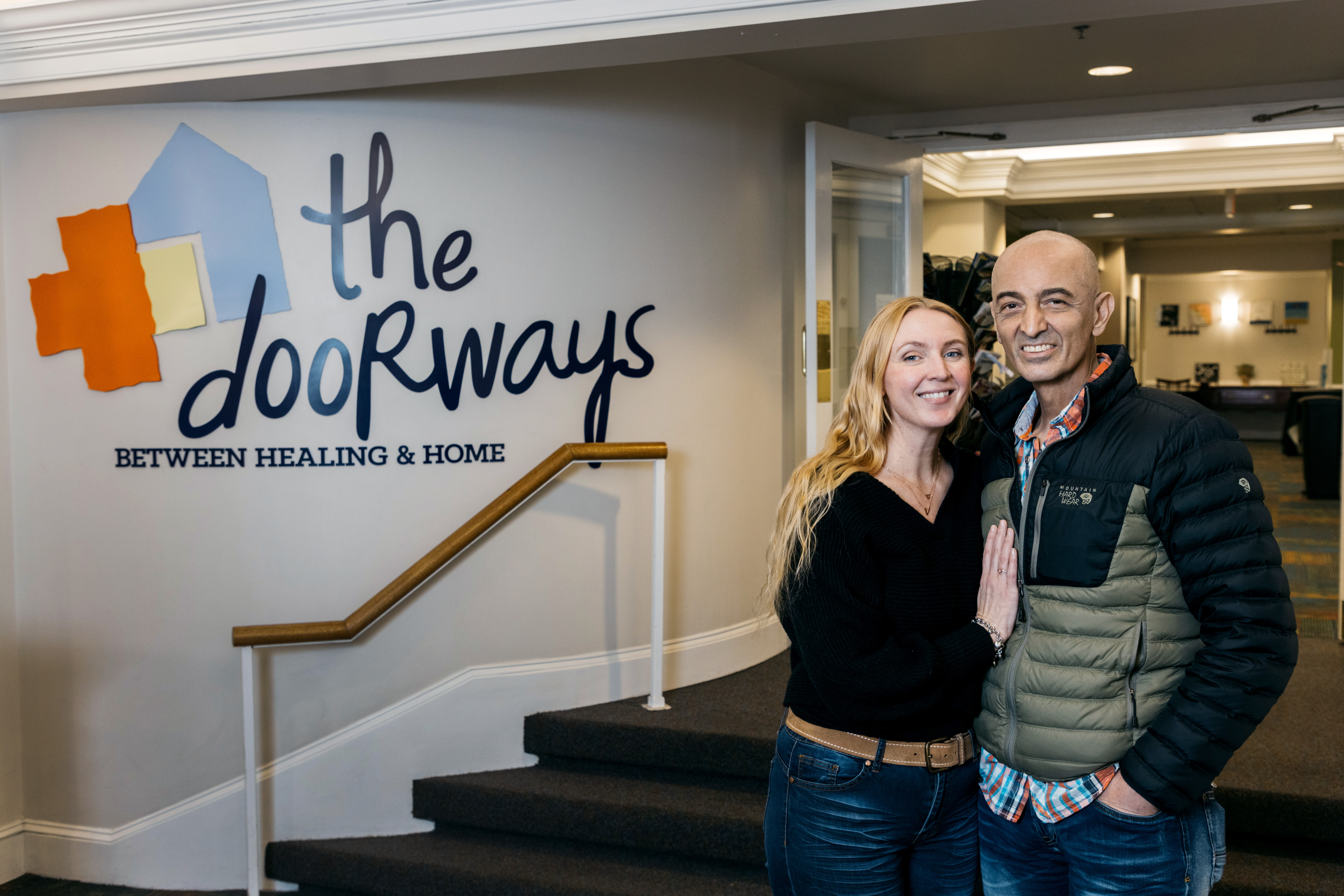 Two smiling adults pose beside The Doorways logo