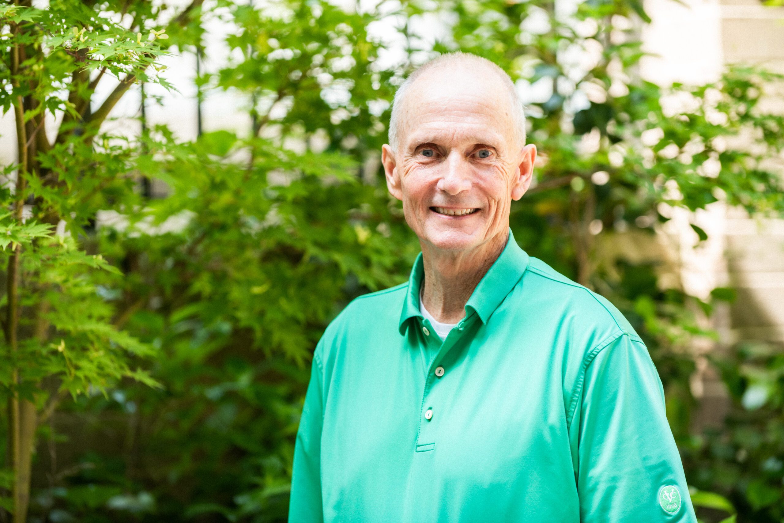 an adult smiles while standing in a lush garden