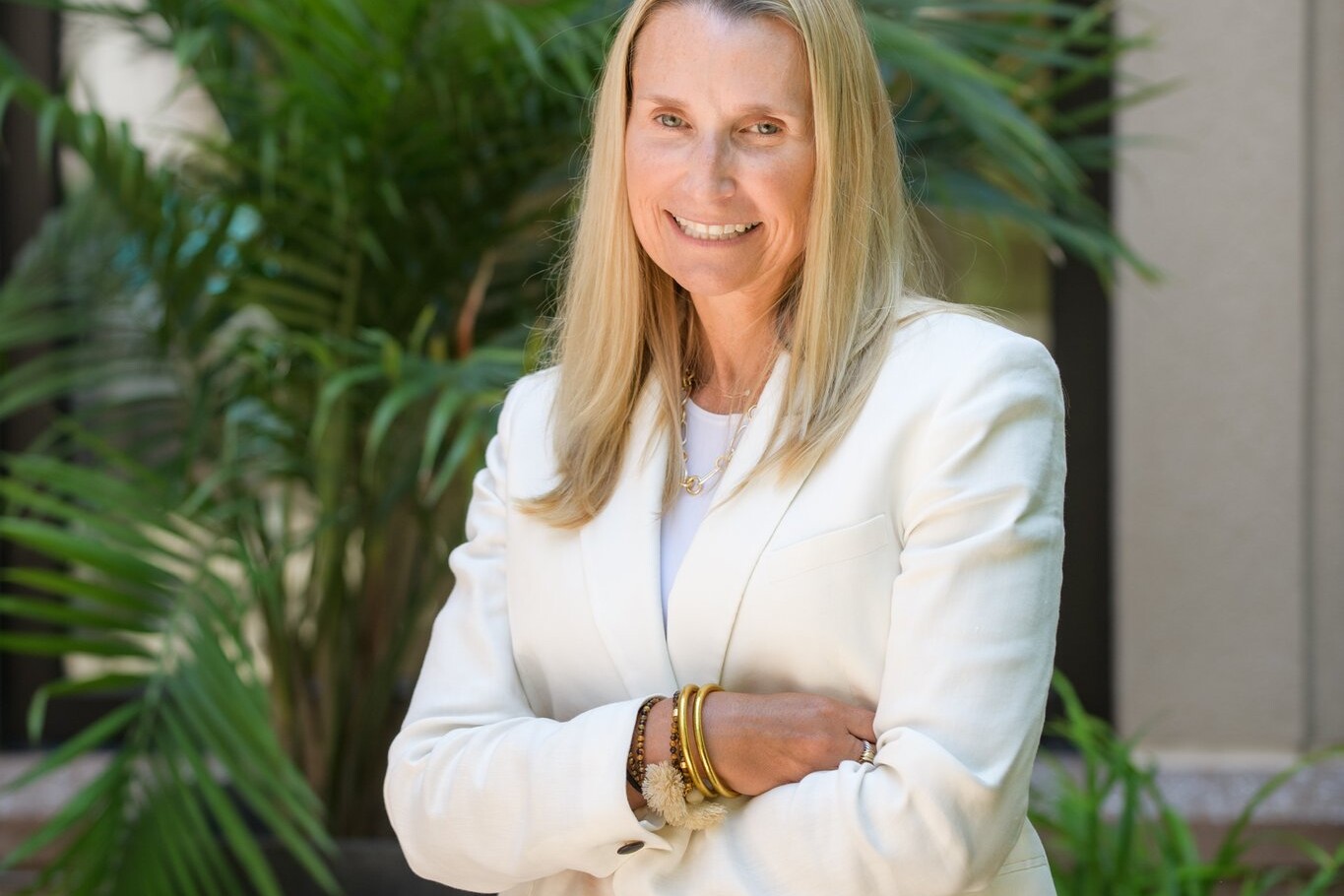 a smiling adult in a white suitcoat stands in a lush garden outside