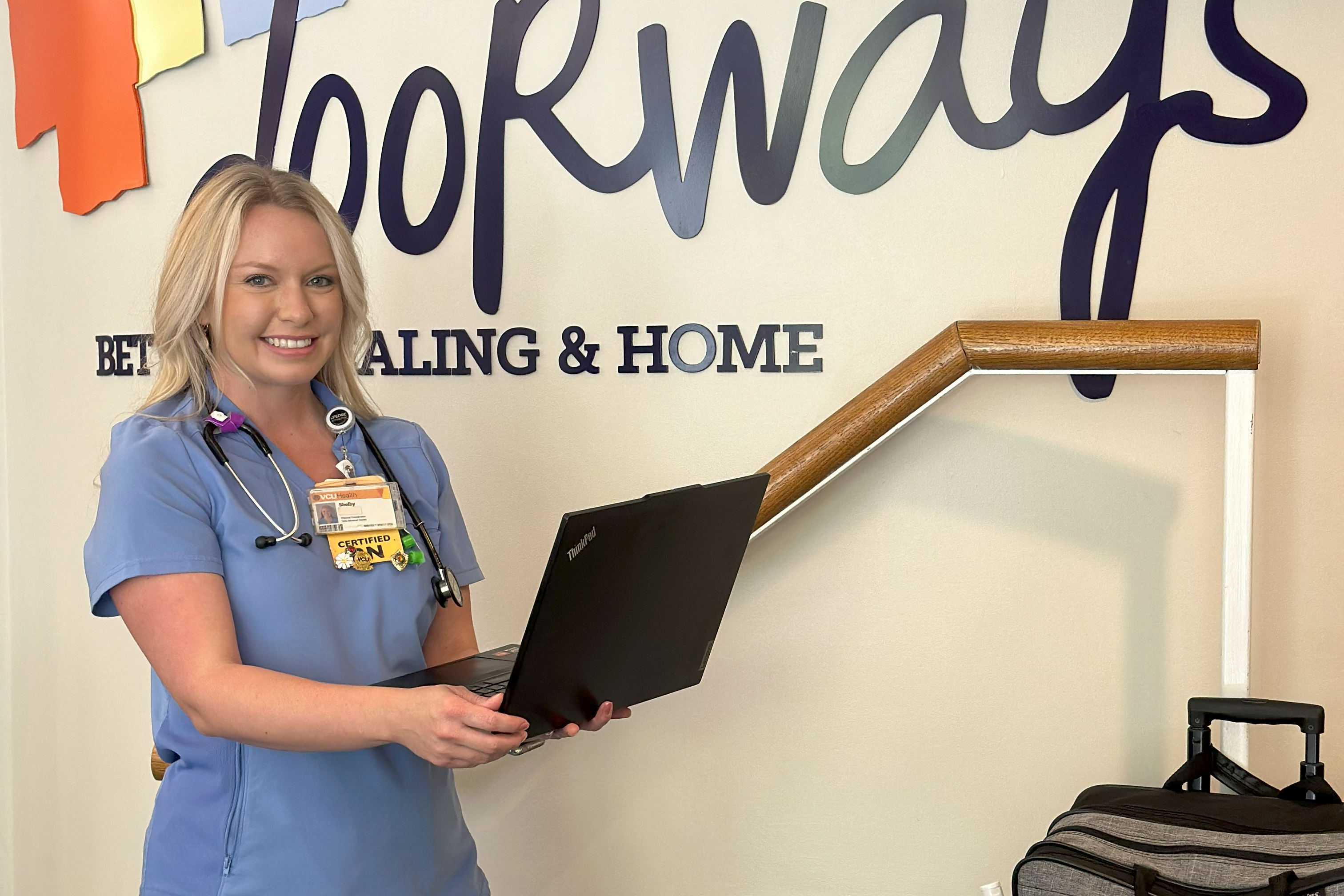 a smiling adult in scrubs holds a laptop with a medical bag in from of The Doorways logo