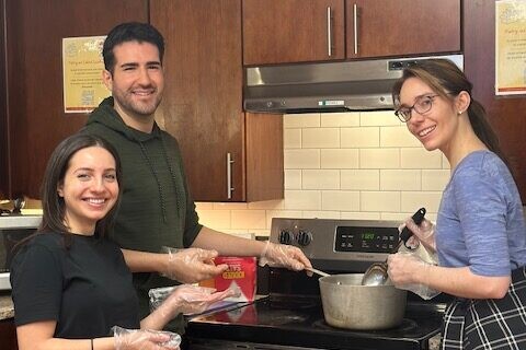 3 smiling adults wearing gloves prepare a meal in the kitchen