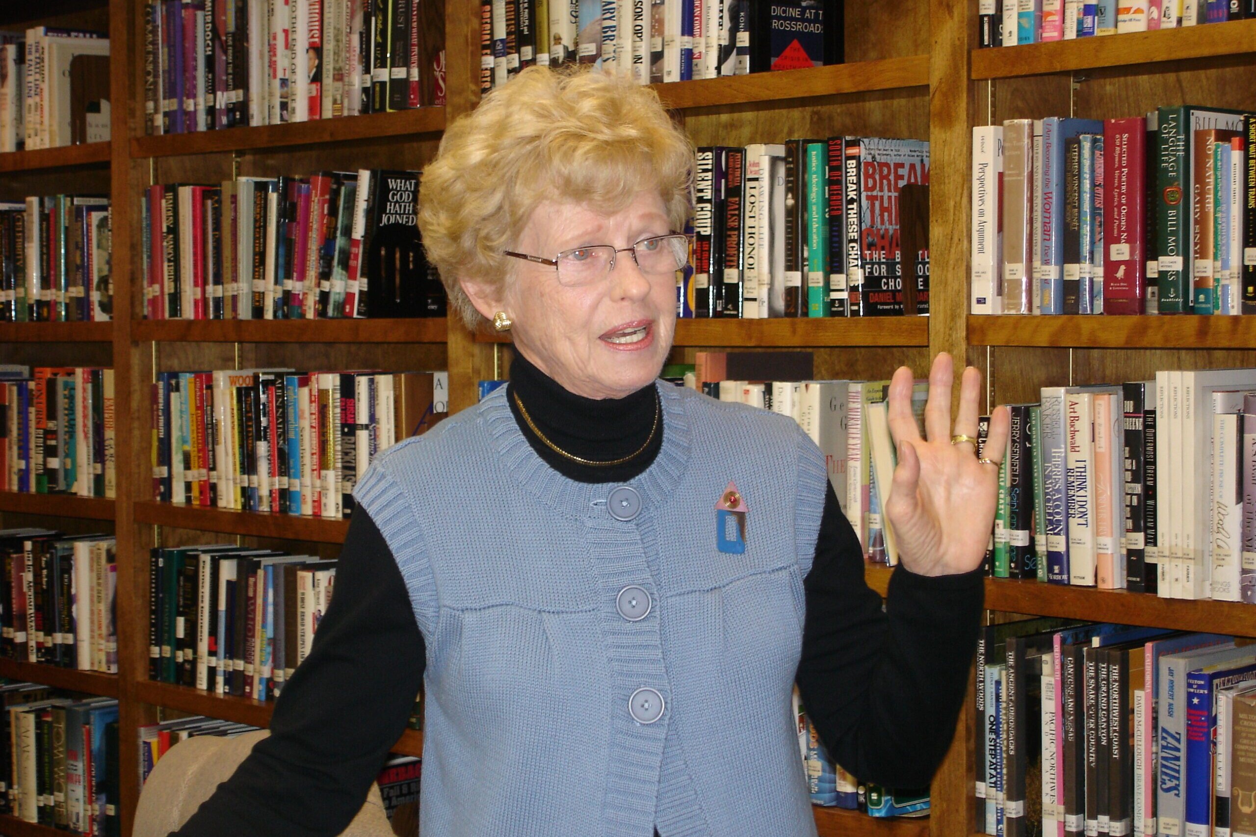 Photo of Dolly Hintz, an adult, smiling and waving in the library of The Doorways