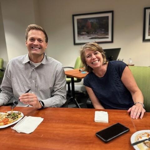 Two smiling staff members sit at the Board Room table