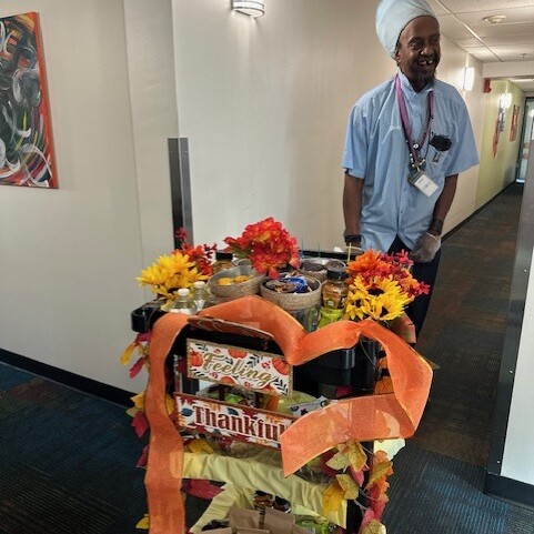 A smiling staff member poses beside the Fun Cart for Housekeeping Week