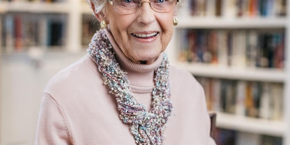 A smiling adult, the incomparable Dolly Hintz, sits in the library at The Doorways