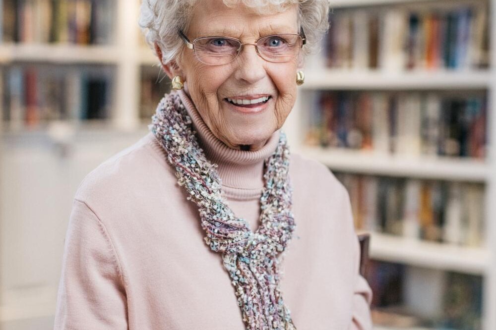 A smiling adult, the incomparable Dolly Hintz, sits in the library at The Doorways