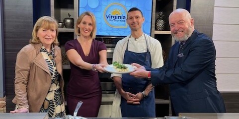 4 smiling adults hold up a beautiful plate of asparagus with the chef behind the dish in a newsroom