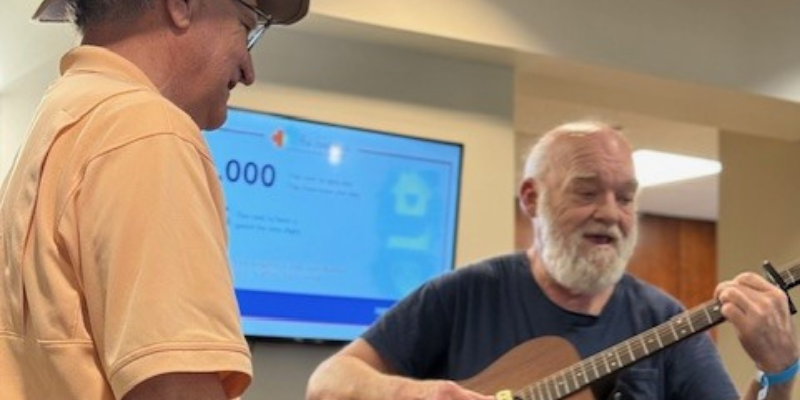 A smiling adult looks on while another guest plays a guitar