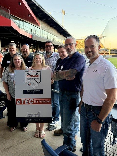 Smiling attendees at the 21st Annual Gilbane Restaurant Walk at CarMax Park with eTec sponsorboard