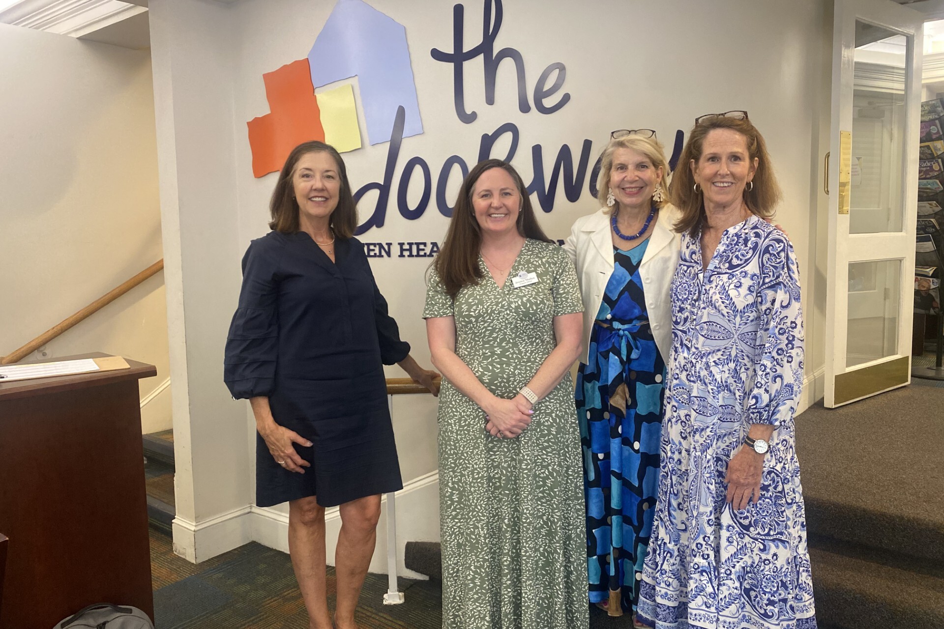 Photo of 4 smiling adults standing in the lobby of The Doorways in front of The Doorways logo