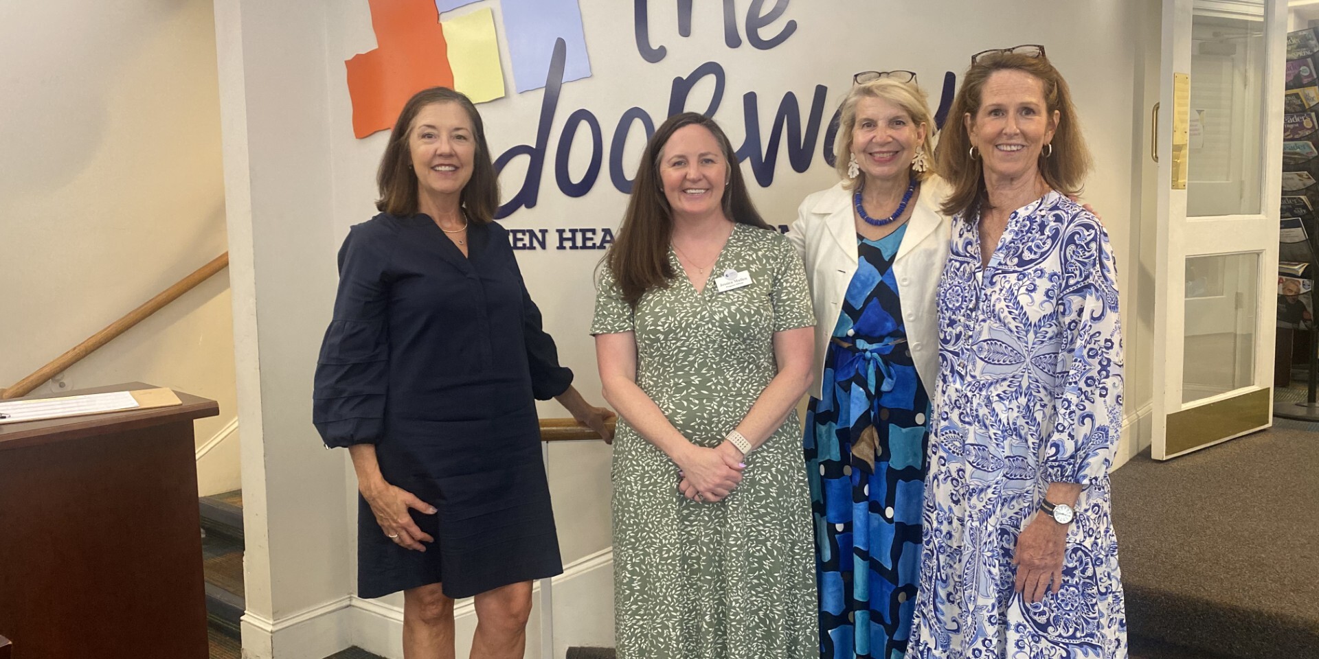 Photo of 4 smiling adults standing in the lobby of The Doorways in front of The Doorways logo