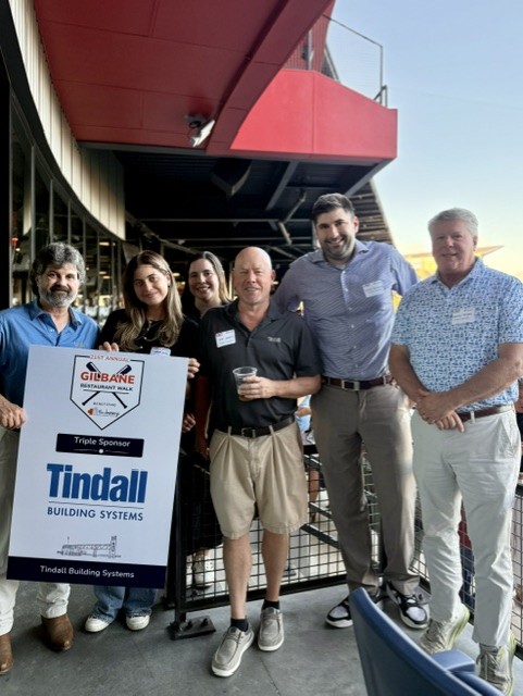 Smiling attendees at the 21st Annual Gilbane Restaurant Walk at CarMax Park with Tindall sponsorboard