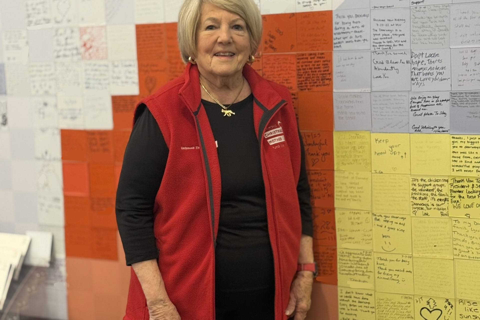 a smiling adult standing by the guest story wall in the lobby of The Doorways