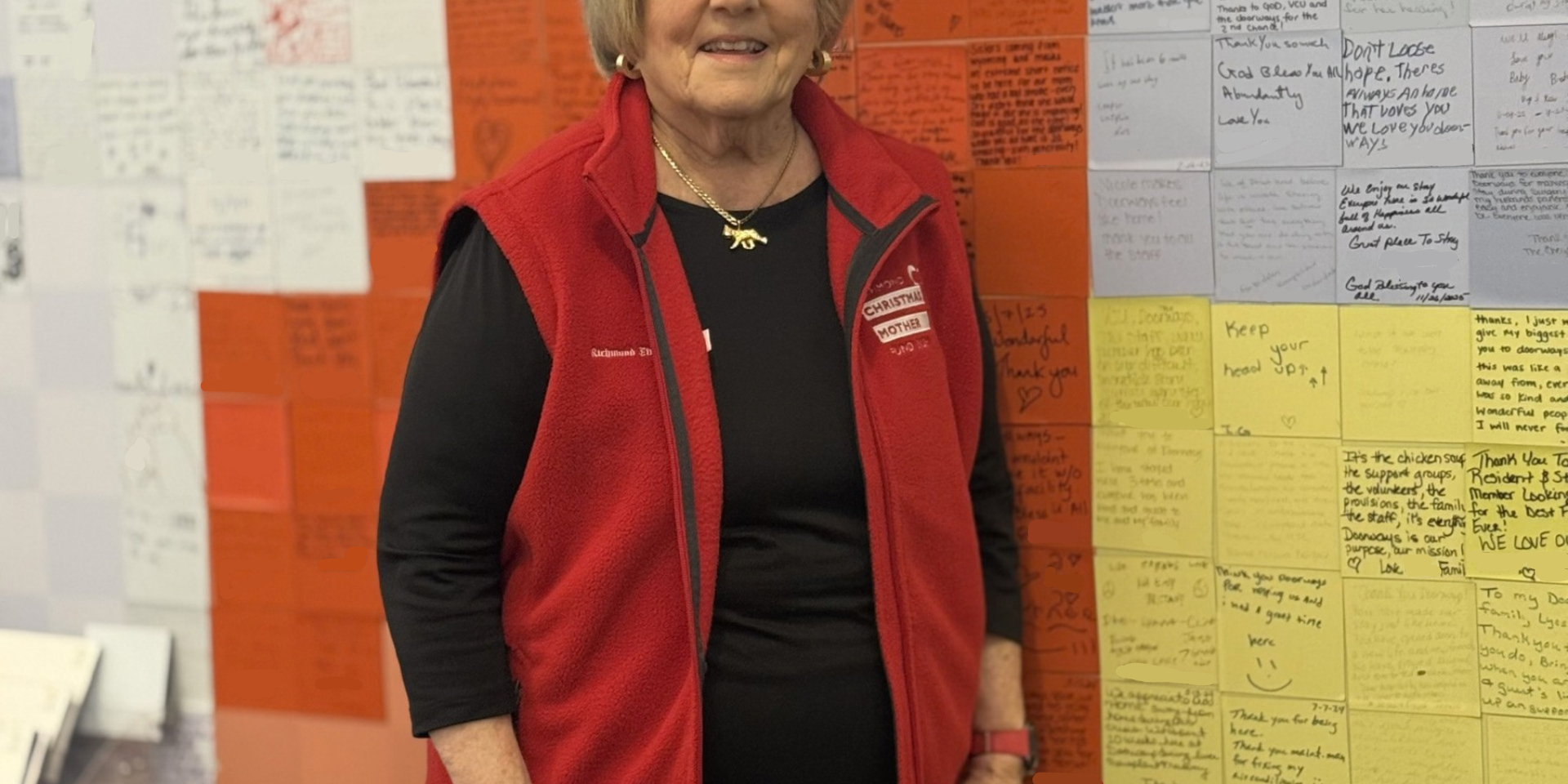 a smiling adult standing by the guest story wall in the lobby of The Doorways